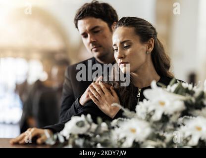 Sad, funeral and flowers with couple and coffin in church for death, respect and mourning. Grief, goodbye and empathy with man and woman loss at Stock Photo