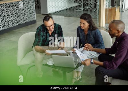 Casual meeting of smiling diverse business team analyzing financial data. Group team discussion in office lobby Stock Photo