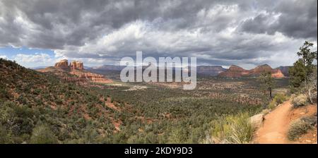 A panoramic view of large fields and Cathedral Rock under a gray cloudy sky in Sedona, Arizona Stock Photo