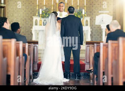 Wedding, priest and couple at the altar for marriage vows in commitment ceremony in a church from behind. Married, love and caring bride and groom Stock Photo