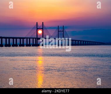 Sun setting behind the support towers of the Prince of Wales Bridge crossing the Severn Estuary between England and Wales UK Stock Photo