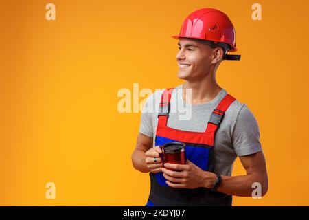 Young builder in uniform holding coffee cup on yellow background Stock Photo