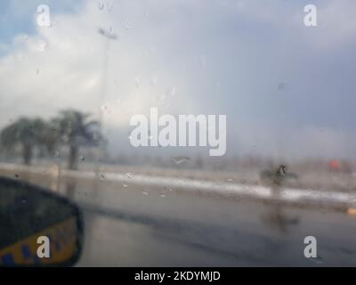 Rain drops on the car window with a view of the exterior mirror and blurred background with palm trees Stock Photo