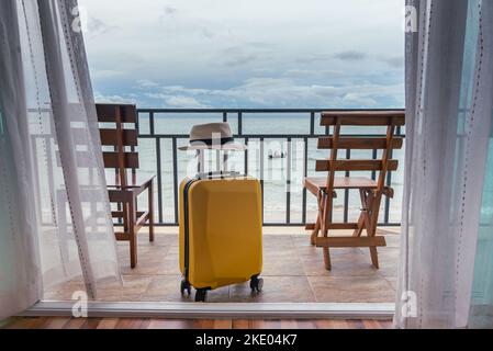 Travel suitcase and hat on the bedroom balcony with sea beach and chair for relaxing background, Travel, vacation concept. Stock Photo