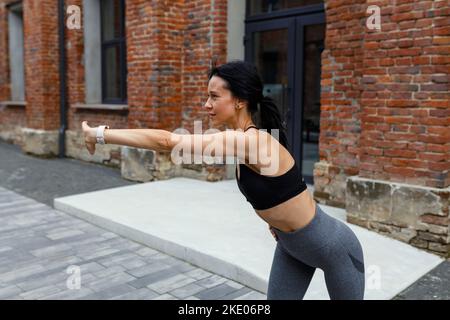 Athlete woman stretches her arms outdoor. Female doing warming up exercise Stock Photo
