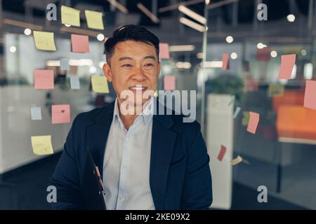 Portrait of handsome asian businessman in suit standing in office and looking away Stock Photo