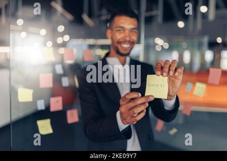 African Businessman showing sticky notes with motivational phrases while standing in office Stock Photo