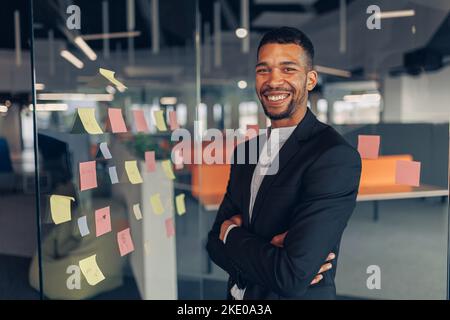 Portrait of smiling african businessman standing in office with crossing hands Stock Photo