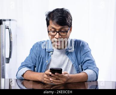 An Indian male with looking at his smart phone with surprised face sitting at home Stock Photo
