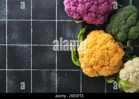 Colorful cauliflower. Various sort of cauliflower on old stone tiles black concrete background. Purple, yellow, white and green color cabbages. Brocco Stock Photo