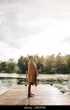 Side view of girl wrapped in towel while standing on jetty Stock Photo