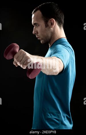 A young man with blue sportswear doing a biceps workout with a light purple-red dumbbell Stock Photo