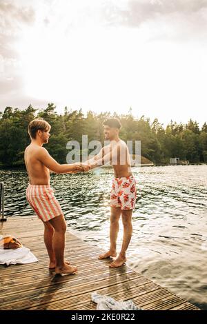 Male friends holding hands while standing on jetty during vacation Stock Photo