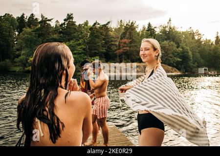 Smiling woman wearing towel while looking at female friend during vacation Stock Photo