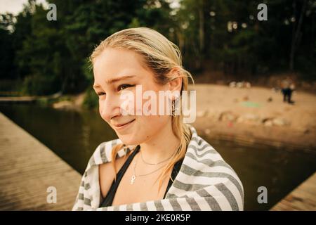 Smiling blond woman wearing towel at lake during vacation Stock Photo