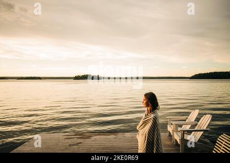 Woman with coffee cup standing on jetty over lake stock photo