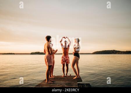 Friends looking at man gesturing while standing on jetty by lake during vacation Stock Photo