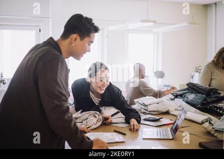 Smiling fashion designer looking at laptop by male colleague at workshop Stock Photo