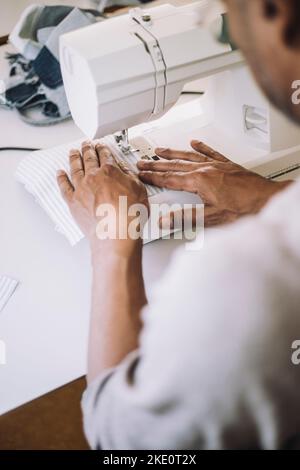Male fashion designer sewing cloth using sewing machine while working at workshop Stock Photo