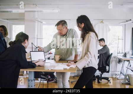 Male and female colleagues discussing over laptop at workshop Stock Photo