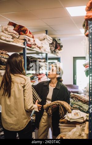 Female fashion designers talking while standing near rack at workshop Stock Photo