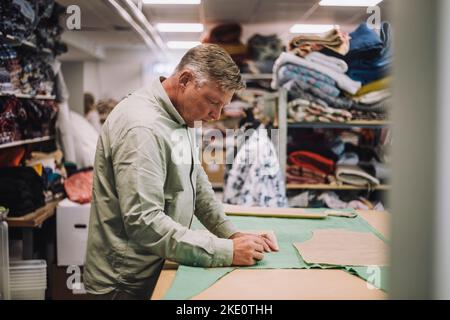 Side view of mature fashion designer marking on fabric while working at workshop Stock Photo