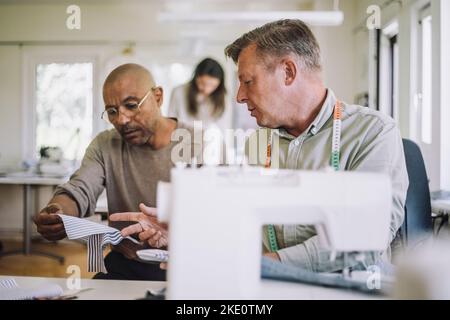 Male design professionals discussing over fabric at workshop Stock Photo