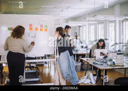 Rear view of fashion designer explaining female colleague while writing on whiteboard at workshop Stock Photo