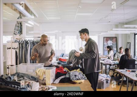 Male fashion designers discussing with each other while sorting recycled clothes at workshop Stock Photo