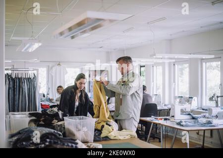 Male and female design professionals sorting out recycled clothes while working at workshop Stock Photo
