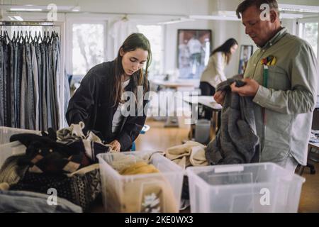 Female fashion designer with male colleague sorting recycled clothes while working at workshop Stock Photo