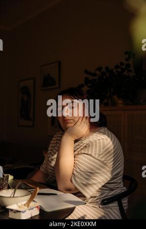 Young woman with eyes closed sitting at table Stock Photo