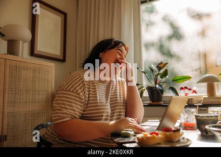 Cheerful young woman covering mouth with hands while sitting at table by window Stock Photo