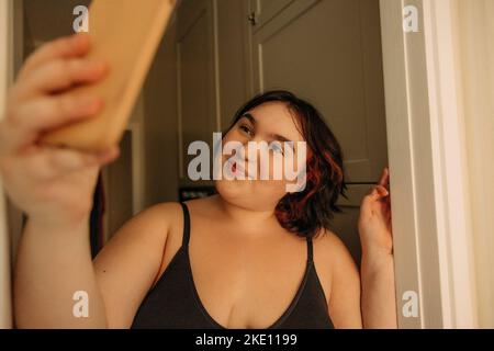 Smiling young woman taking selfie through mobile phone at home Stock Photo