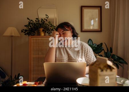 Cheerful young woman sitting using laptop at home Stock Photo