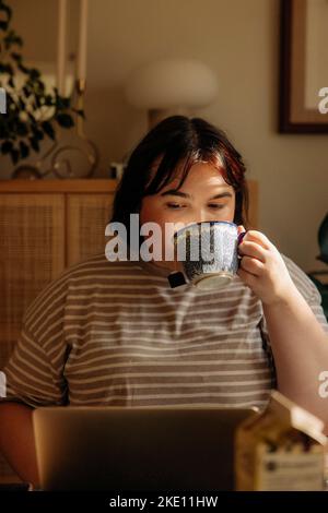 Young woman drinking coffee while using laptop at home Stock Photo