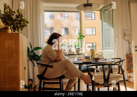 Young woman talking on smart phone while sitting on chair at home Stock Photo