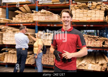 Portrait of smiling salesman holding glove while standing in front of rack at hardware store Stock Photo