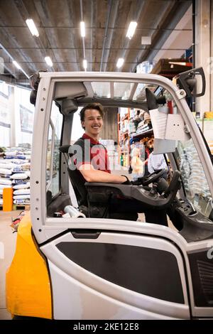 Side view of male warehouse worker sitting in forklift at warehouse Stock Photo