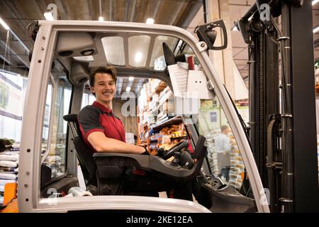 Smiling warehouse worker sitting in forklift at warehouse Stock Photo