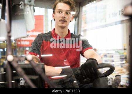 Young male warehouse worker driving forklift in warehouse seen through windshield Stock Photo