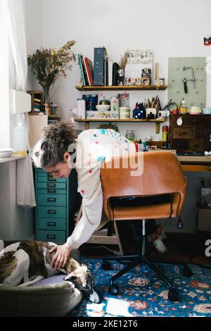 Woman stroking dog while sitting on chair at home Stock Photo