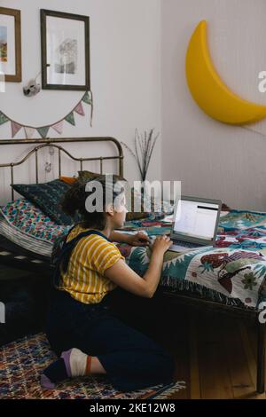 Woman using laptop while sitting near bed at home Stock Photo