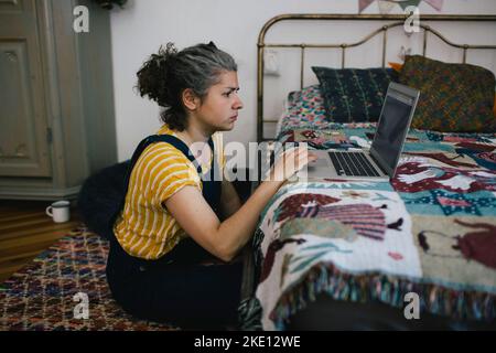 Woman sitting on floor using laptop in bedroom at home Stock Photo