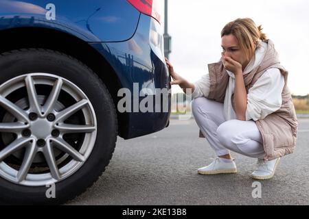 frustrated woman next to car examines bumper damage Stock Photo