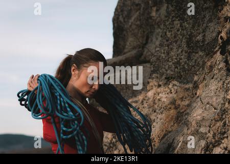 A woman in a red shirt holding a rope to rock climbing on a sunny day. Stock Photo