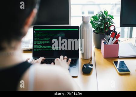 Non-binary programmer coding over laptop while working in startup company Stock Photo