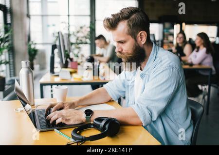 Concentrated male programmer typing on laptop while working in startup company Stock Photo