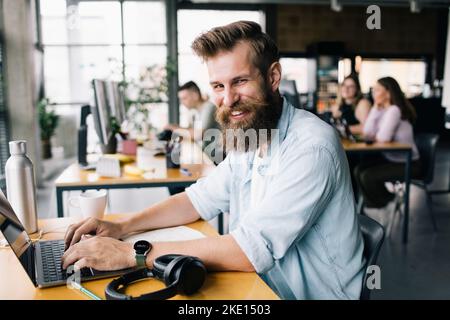 Portrait of smiling male computer programmer typing on laptop while working in office Stock Photo