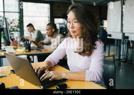 Female computer programmer coding on laptop at desk in startup company Stock Photo